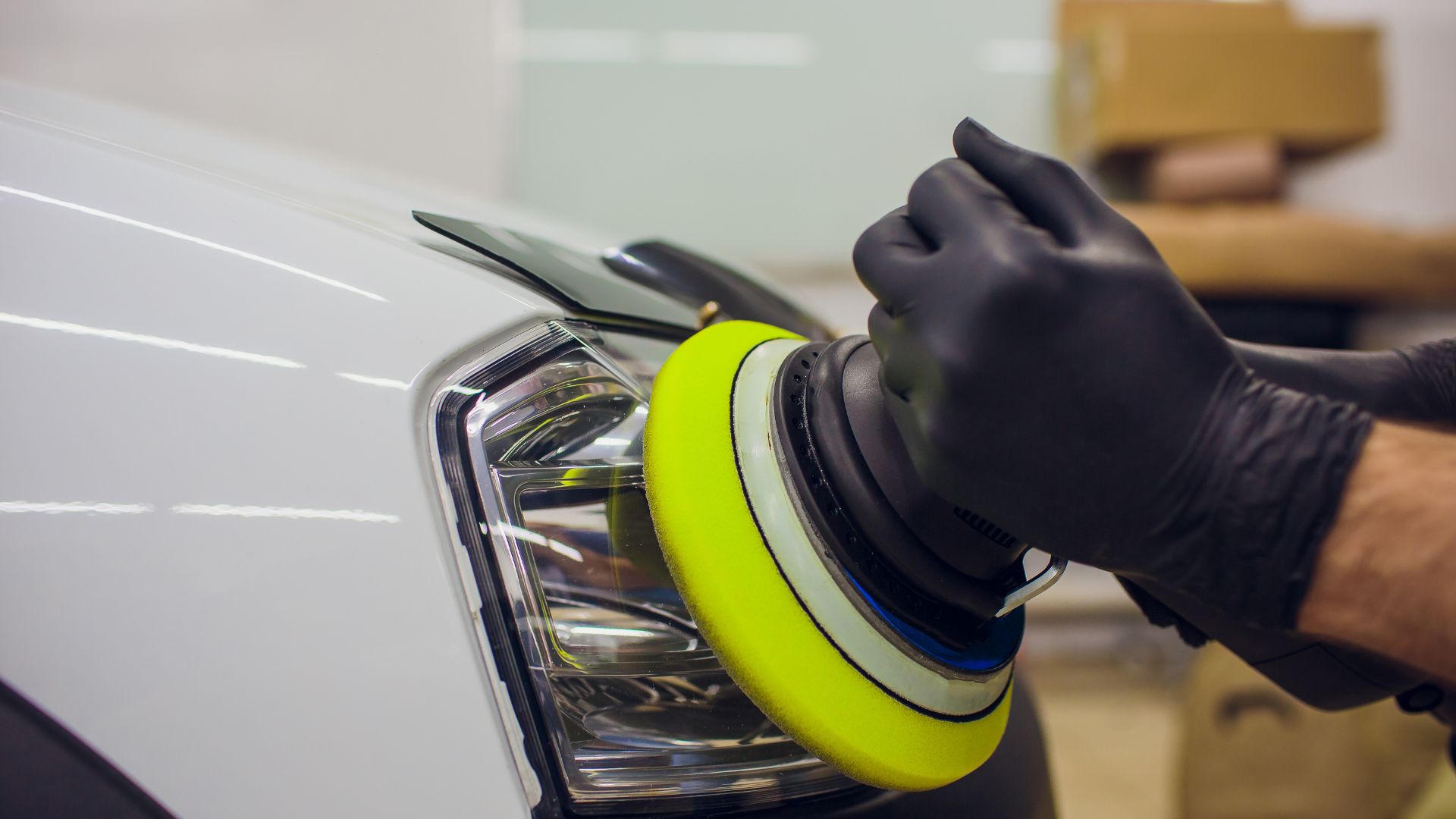 Buffing car headlight with yellow polishing pad and black gloved hand
