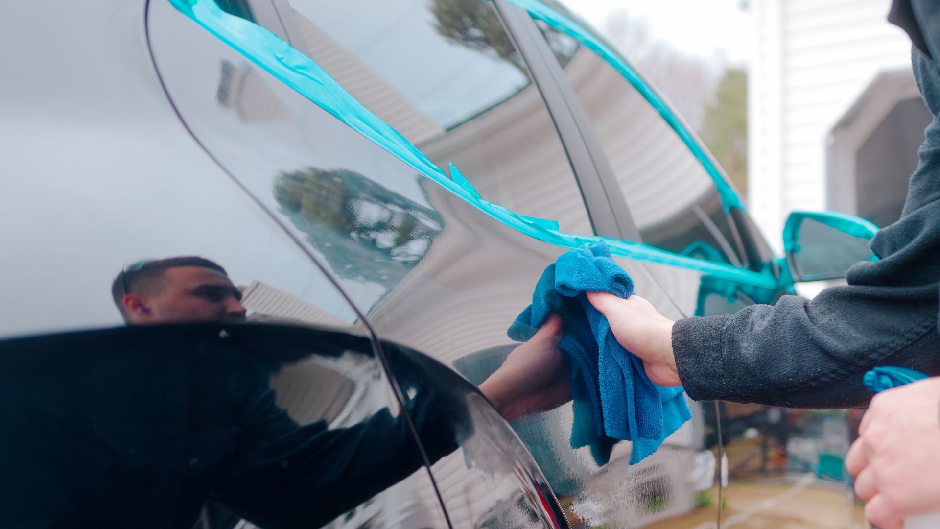 Hand washing car with blue microfiber cloth and turquoise cleaning tool