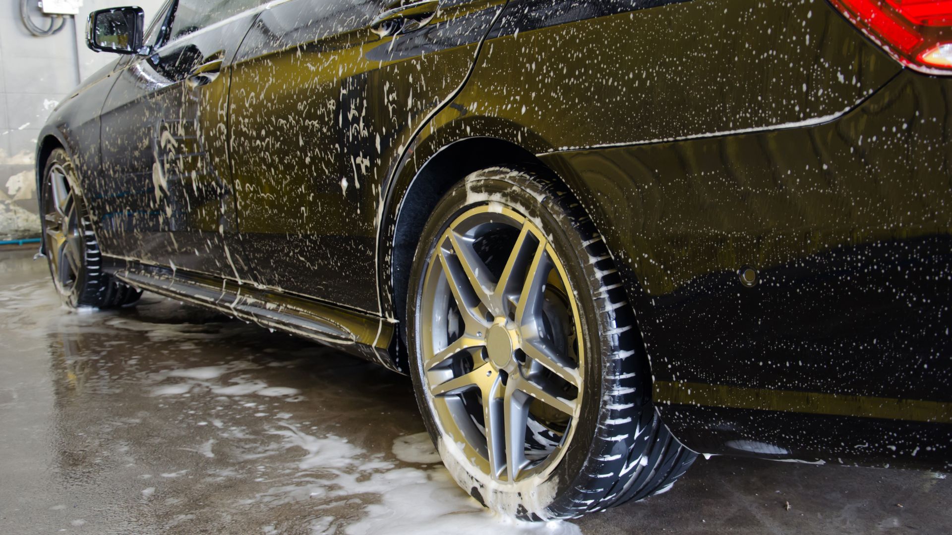 Wet dark car with water droplets and foam during car wash