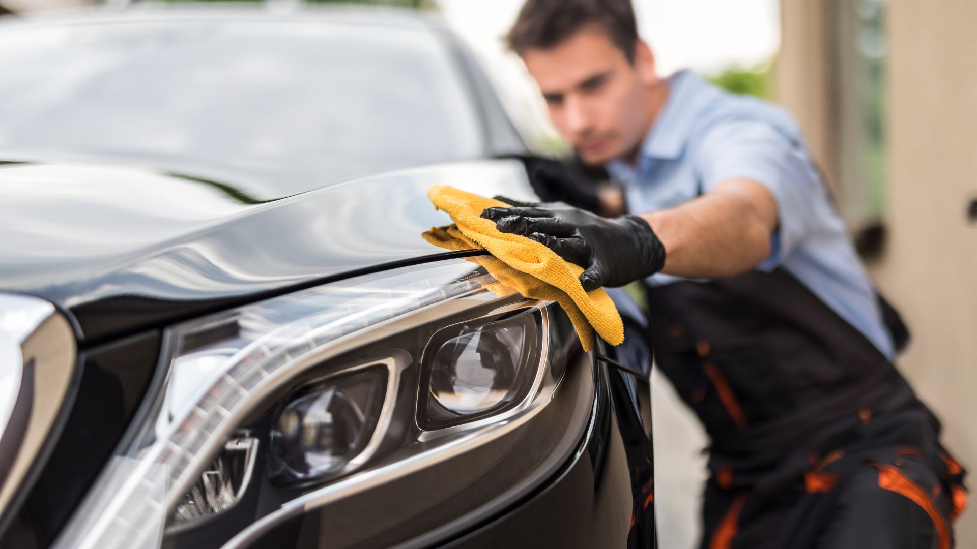 Car detailing with yellow microfiber cloth, polishing sleek black vehicle