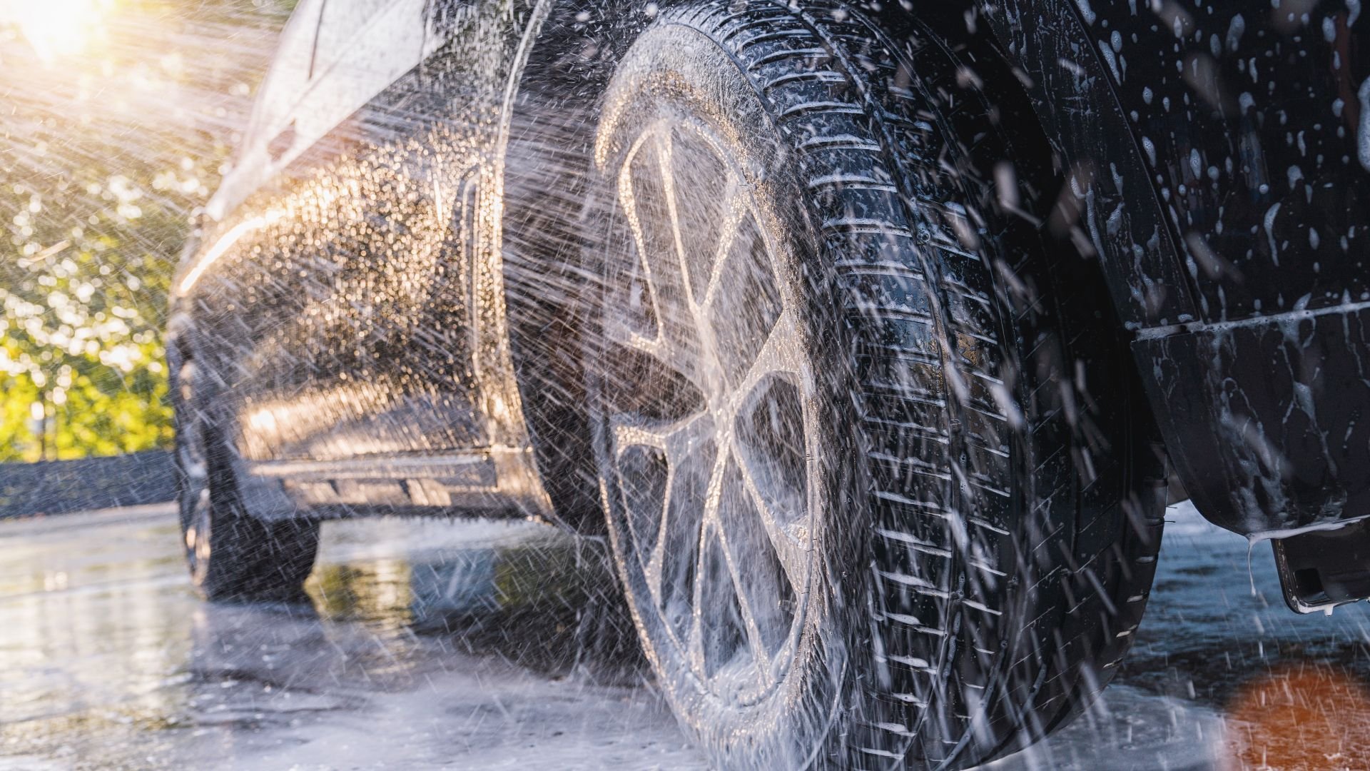 Car wheel splashing water during car wash with sunlight in background