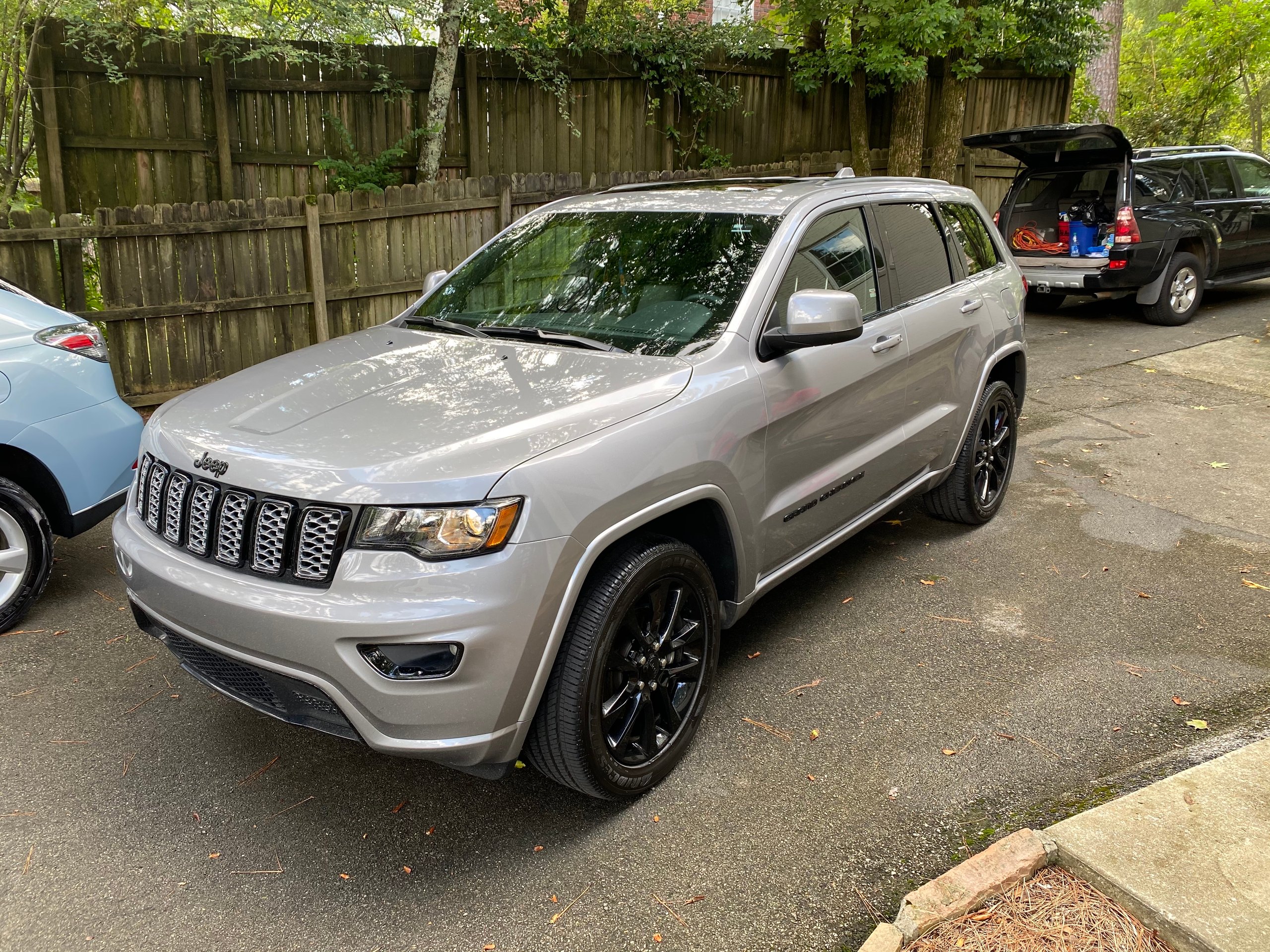 Silver Jeep Grand Cherokee parked in driveway with wooden fence