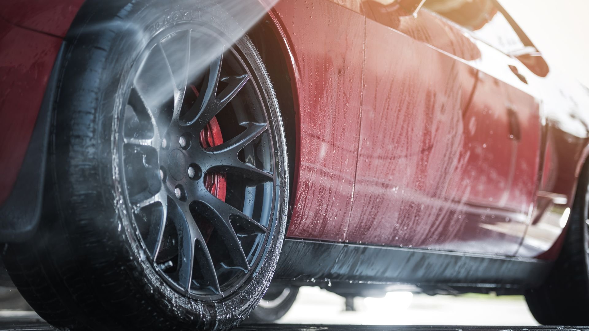 Wet red car with black alloy wheel and water droplets